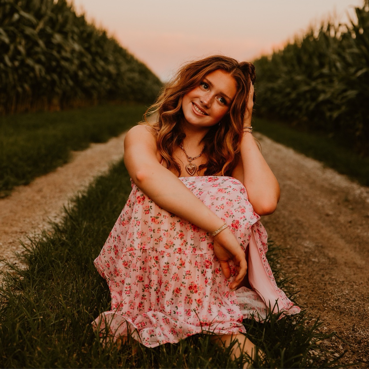 Stella Mabry seated on a country lane in a pink floral dress at sunset.